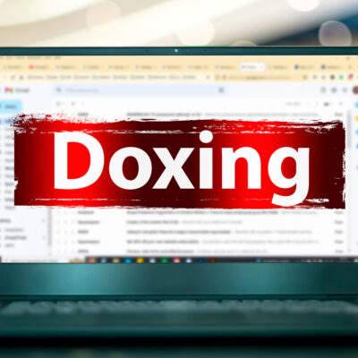 Ein aufgeklappter Laptop mit geöffnetem E-Mail-Programm. Davor ist das Wort "Doxing" mit warnend rotem Hintergrund.