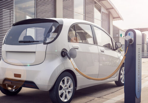 ein weißes Elektroauto wird bei Sonnenschein an einer Ladesäule aufgeladen.