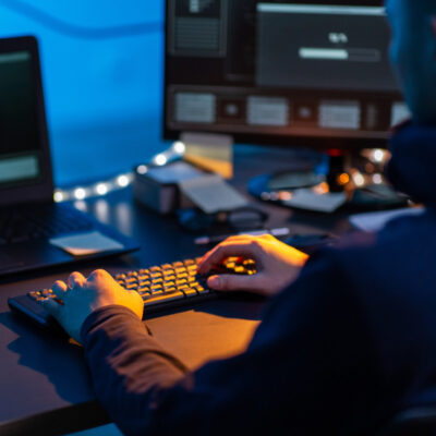 Person sitzt in einem dunklen Raum am PC und tippt auf der Tastatur.