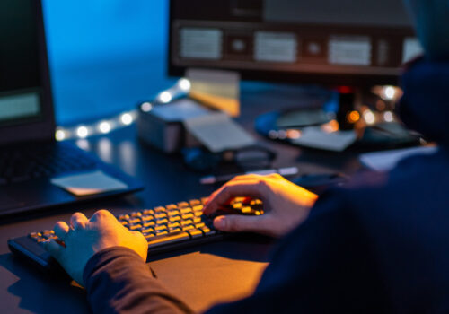 Person sitzt in einem dunklen Raum am PC und tippt auf der Tastatur.