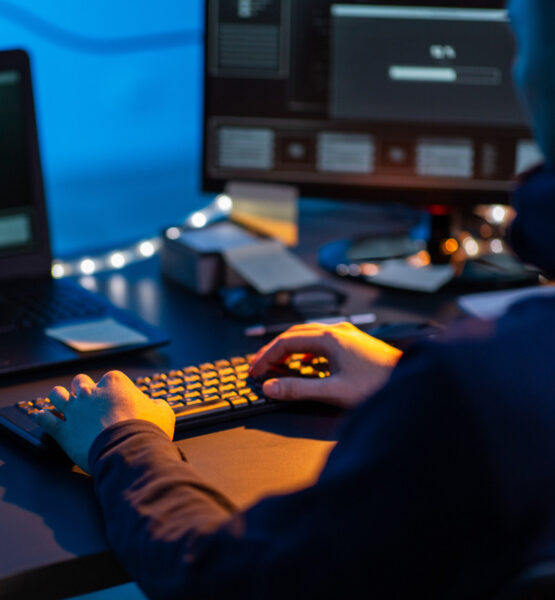 Person sitzt in einem dunklen Raum am PC und tippt auf der Tastatur.