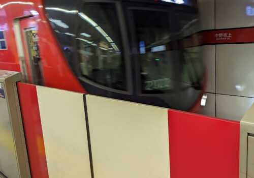 eine rote U-Bahn fährt in einen Bahnsteig ein. DIe Zugänge sind mit Barrieren abgesichert.
