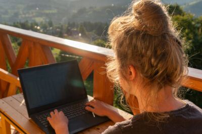 Eine Frau arbeitet gemütlich auf einer Dachterasse, umgeben von schöner Natur und Sonnenschein.