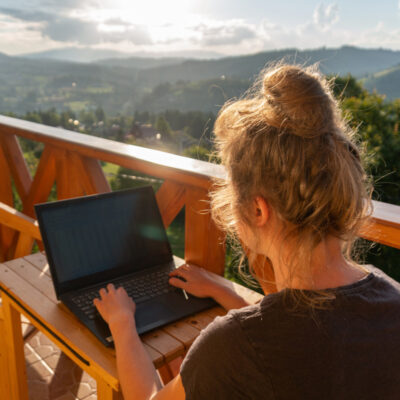 Eine Frau arbeitet gemütlich auf einer Dachterasse, umgeben von schöner Natur und Sonnenschein.