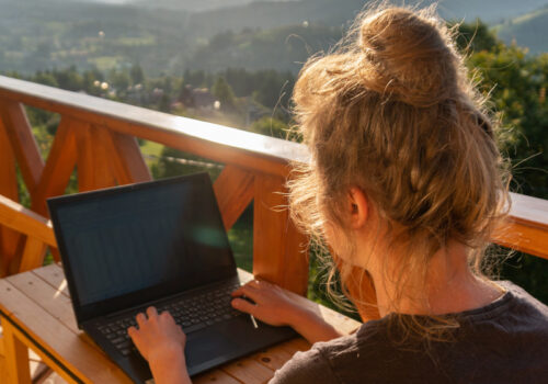 Eine Frau arbeitet gemütlich auf einer Dachterasse, umgeben von schöner Natur und Sonnenschein.
