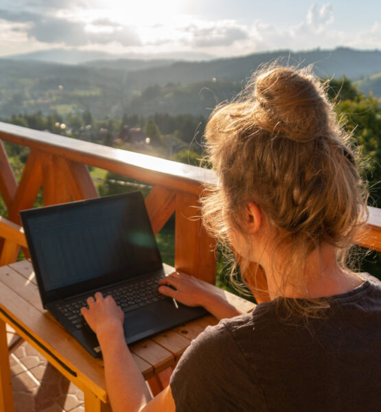 Eine Frau arbeitet gemütlich auf einer Dachterasse, umgeben von schöner Natur und Sonnenschein.