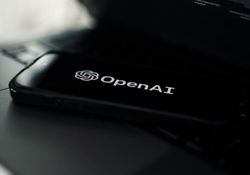 Ein Smartphone auf einem Laptop. Auf dem Smartphone-Bildschirm ist das Logo von Open AI zu sehen.