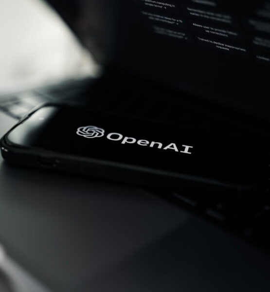 Ein Smartphone auf einem Laptop. Auf dem Smartphone-Bildschirm ist das Logo von Open AI zu sehen.