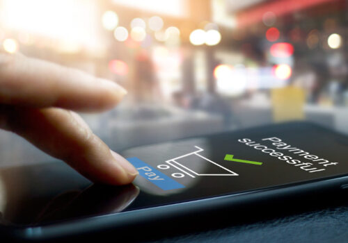 jemand bedient ein Smartphone auf einem Tisch. Auf dem Display sieht man die Bestätigung für eine erfolgreiche Bezahlung.