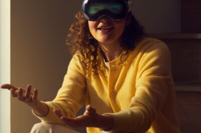 Eine junge Frau sitzt auf einer Treppenstufe und trägt eine Apple Vision Pro. Ihre Augen sind über das Front-Display zu erkennen.