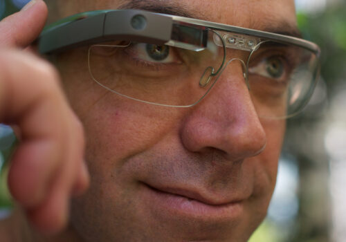 Ein Mann trägt eine Google Glass-Brille und bedient sie mit einem Finger am Rahmen.