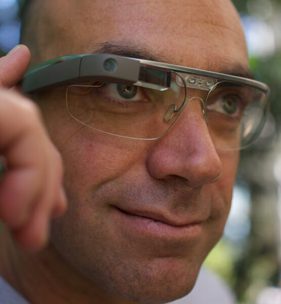 Ein Mann trägt eine Google Glass-Brille und bedient sie mit einem Finger am Rahmen.