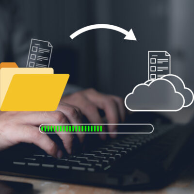 Datentransfer dargestellt von einem Ordner- und einem Cloudsymbol, einem Pfeil zwischen den beiden und einem Ladebalken. Im Hintergrund sieht man Hände auf einer Tastatur.