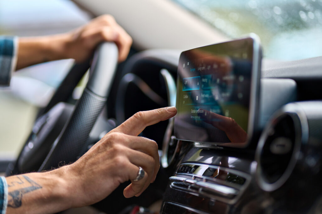 Eine Hand am Lenkrad, nutzt ein Autofahrer mit der anderen sein digitales Navigationssystem per Touchscreen.