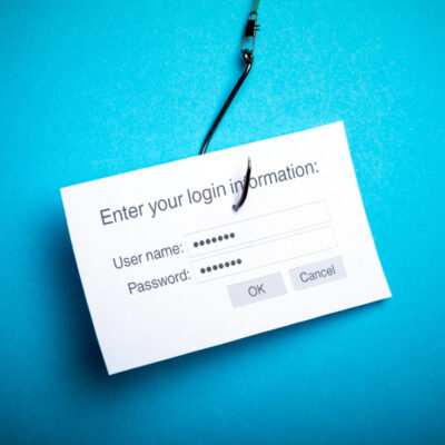 Ein Bild von einem weißen Papier auf einem blauen Hintergrund, das ein Login-Formular darstellt mit Feldern für "User name" und "Password". Über dem Formular steht "Enter your login information:". Das Papier hat einen Angelhaken durchstochen, was auf den Begriff "Phishing" anspielt.