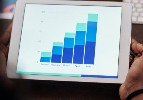 Eine Person hält ein Tablet in der Hand, auf dem ein nicht weiter spezifiziertes Säulendiagramm für die Monate Januar bis Mai zu sehen ist.