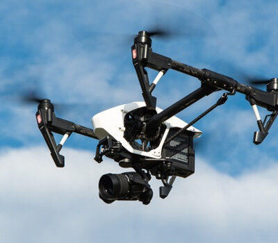 Privatdrohne mit Kamera fliegt durch die Luft. Leicht bewölkter Himmel im Hintergrund.