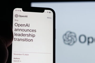 Ein Smartphone, das in der Hand gehalten wird, zeigt einen Blogbeitrag von OpenAI mit der Überschrift "OpenAI announces leadership transition" auf dem Bildschirm. Impliziert werden Veränderungen in der KI-Entwicklung. Im Hintergrund ist unscharf das Logo von OpenAI auf einem größeren Bildschirm zu sehen. Es ist dunkel um das Telefon herum, was den Bildschirminhalt hervorhebt.