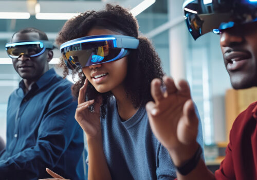Drei Personen tragen Virtual Reality, Augmented Reality oder Extended Reality-Brillen und interagieren mit virtuellen Elementen, die nur sie sehen können. Sie scheinen konzentriert und eingebunden in die Technologieerfahrung, die ihnen die Brillen bieten. Das Foto spielt in einem modernen Büro oder Labor und nutzt künstliches Licht, um eine technologieorientierte Atmosphäre zu schaffen.