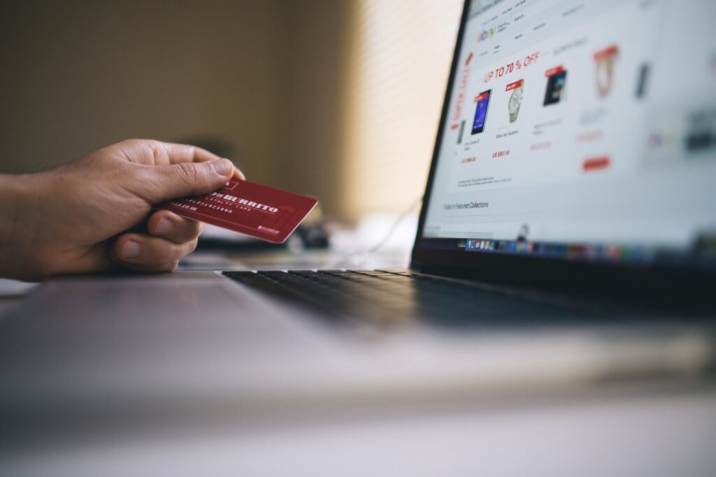 Eine Hand hält eine rote Kreditkarte über eine Laptop-Tastatur, im Hintergrund ist ein unscharfer Online-Shopping-Webseite auf dem Bildschirm zu sehen.





