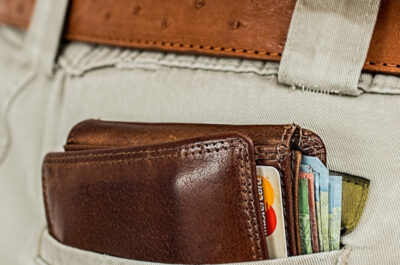 Ein braunes Lederportemonnaie mit Kreditkarten und Bargeld steckt in der hinteren Tasche einer beigen Hose, die mit einem braunen Ledergürtel getragen wird.