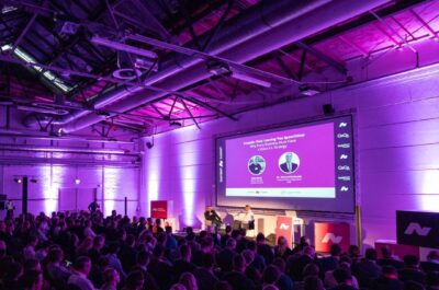 Blick auf eine von violettem Licht beleuchtete Bühne des Chatbot Summit, auf der ein Fireside-Chat vor großen Publikum stattfindet.