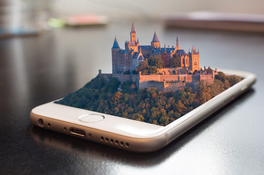 Ein Smartphone liegt auf einem Tisch aus dessen Bildschirm die holographische Projektion einer majestätischen Burg auf einem bewaldeten Hügel herauswächst. Das Bild auf dem Smartphone zeigt die Burg in lebendigen Farben während der Dämmerung, was eine moderne Art der Präsentation von Reisezielen oder historischen Stätten suggeriert.