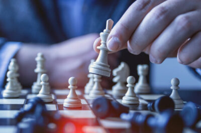 Eine Person die nicht genauer erkennbar ist spielt eine weiße Schachfigur auf einem Schachbrett.