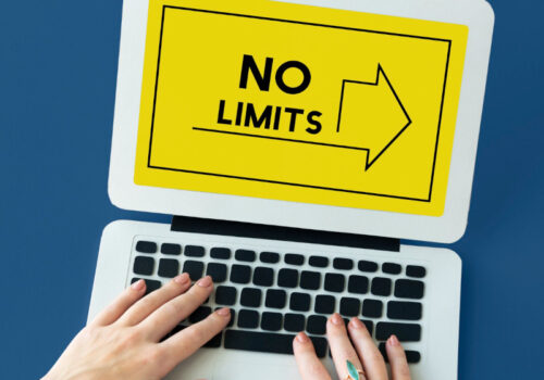 Hände auf der Tastatur eines Laptops auf dessen Bildschirm mit gelben Hintergrund eine Grafik ist deren Aufschrift "No Limits" verspricht.