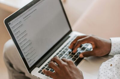Ein Mann hat einen Laptop auf dem Schoss und tippt darin etwas ein. Symbolbild für die Arbeit mit Domainendungen
