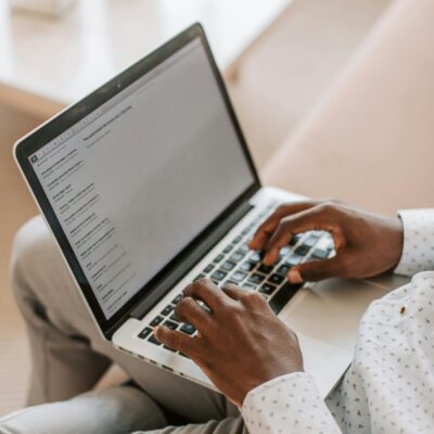 Ein Mann hat einen Laptop auf dem Schoss und tippt darin etwas ein. Symbolbild für die Arbeit mit Domainendungen