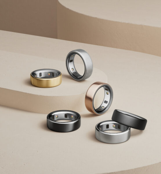 Ein stilvoll arrangiertes Set aus sechs modernen Smart-Ringen in verschiedenen Metallfarben – darunter Gold, Schwarz, Silber, Roségold und gebürstetes Grau – auf einer minimalistischen beigen Stufenplattform. Die Ringe sind mit eingebauten Sensoren auf der Innenseite ausgestattet und reflektieren einen eleganten, technologischen Look. Die Komposition betont die luxuriöse Verarbeitung und die Vielseitigkeit der Smart-Ringe als modische Wearables.