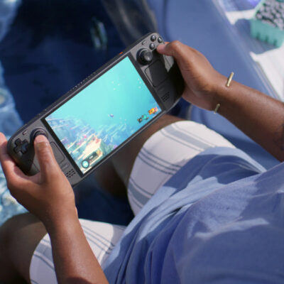 Ein Mann spielt auf dem Steam Deck OLED ein Spiel, das unter Wasser stattfindet, während er selbst an einem Pool sitzt und die Füße im Wasser hat.