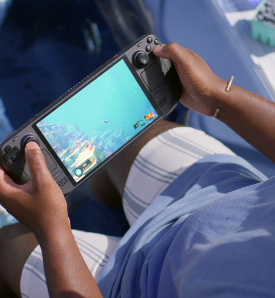 Ein Mann spielt auf dem Steam Deck OLED ein Spiel, das unter Wasser stattfindet, während er selbst an einem Pool sitzt und die Füße im Wasser hat.