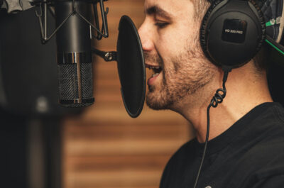 Ein Mann mit Kopfhörern steht an einem Studiomikrofon und spricht hinein.