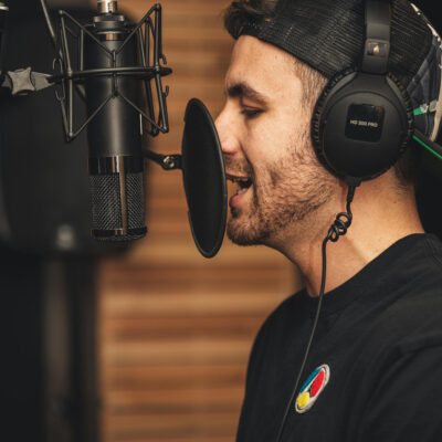 Ein Mann mit Kopfhörern steht an einem Studiomikrofon und spricht hinein.