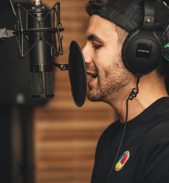 Ein Mann mit Kopfhörern steht an einem Studiomikrofon und spricht hinein.