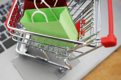 Ein Miniatur-Einkaufswagen gefüllt mit Miniatur-Einkaufstaschen steht auf dem Touchpads eines Laptops.