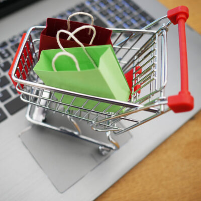 Ein Miniatur-Einkaufswagen gefüllt mit Miniatur-Einkaufstaschen steht auf dem Touchpads eines Laptops.