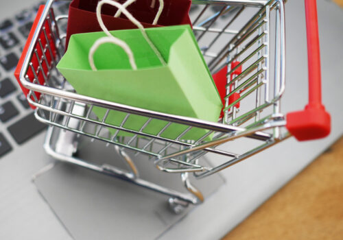 Ein Miniatur-Einkaufswagen gefüllt mit Miniatur-Einkaufstaschen steht auf dem Touchpads eines Laptops.