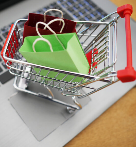 Ein Miniatur-Einkaufswagen gefüllt mit Miniatur-Einkaufstaschen steht auf dem Touchpads eines Laptops.