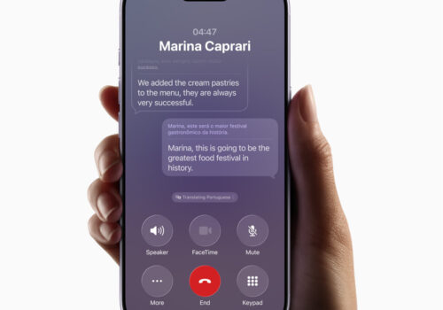 Eine Hand hält ein iPhone, auf der eine Kommunikations-App geöffnet ist, deren Nachrichten mit KI-Unterstützung ins Englische übersetzt werden.
