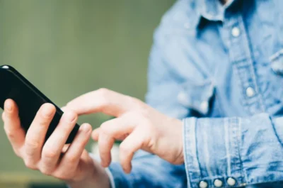 Eine Person sitzt draußen mit seinem Smartphone in der Hand und schaut sich auf diesem etwas an.