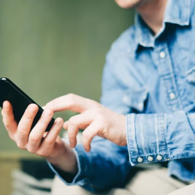 Eine Person sitzt draußen mit seinem Smartphone in der Hand und schaut sich auf diesem etwas an.