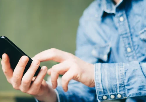 Eine Person sitzt draußen mit seinem Smartphone in der Hand und schaut sich auf diesem etwas an.