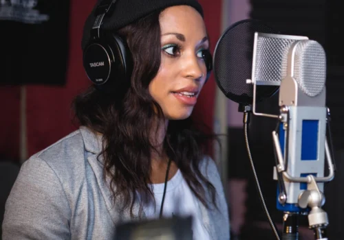 Eine Frau steht mit Kopfhörer vor einem Mikrofon im Aufnahmestudio.