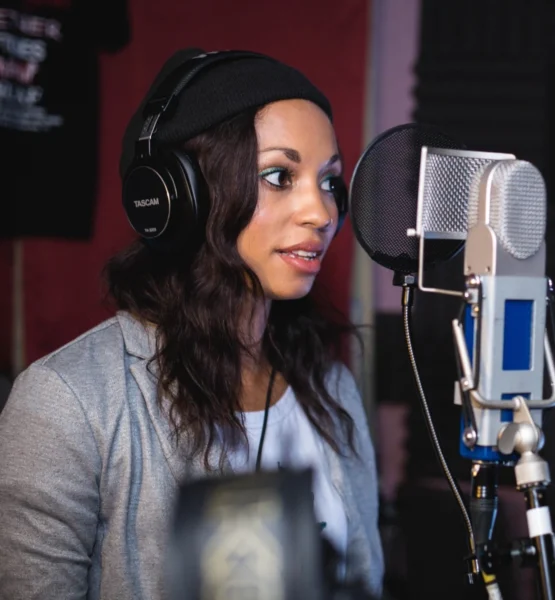 Eine Frau steht mit Kopfhörer vor einem Mikrofon im Aufnahmestudio.