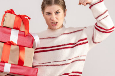 Eine Frau hält in einer Hand mehrere Geschenke und spannt den Bizeps des anderen Arms an.