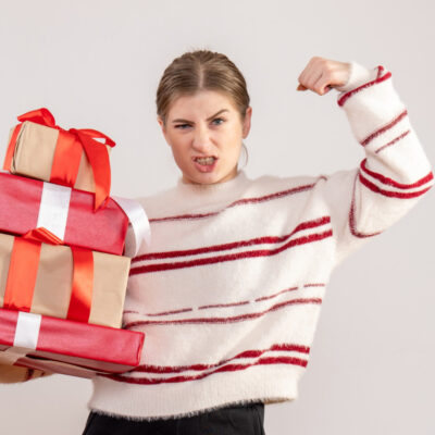 Eine Frau hält in einer Hand mehrere Geschenke und spannt den Bizeps des anderen Arms an.