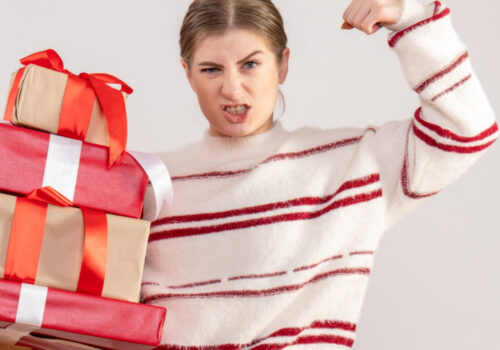 Eine Frau hält in einer Hand mehrere Geschenke und spannt den Bizeps des anderen Arms an.